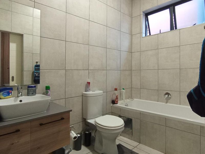 A modern bathroom featuring a vessel sink vanity, a bathtub, and neutral floor-to-ceiling wall tiles with a top-hung window for ventilation.