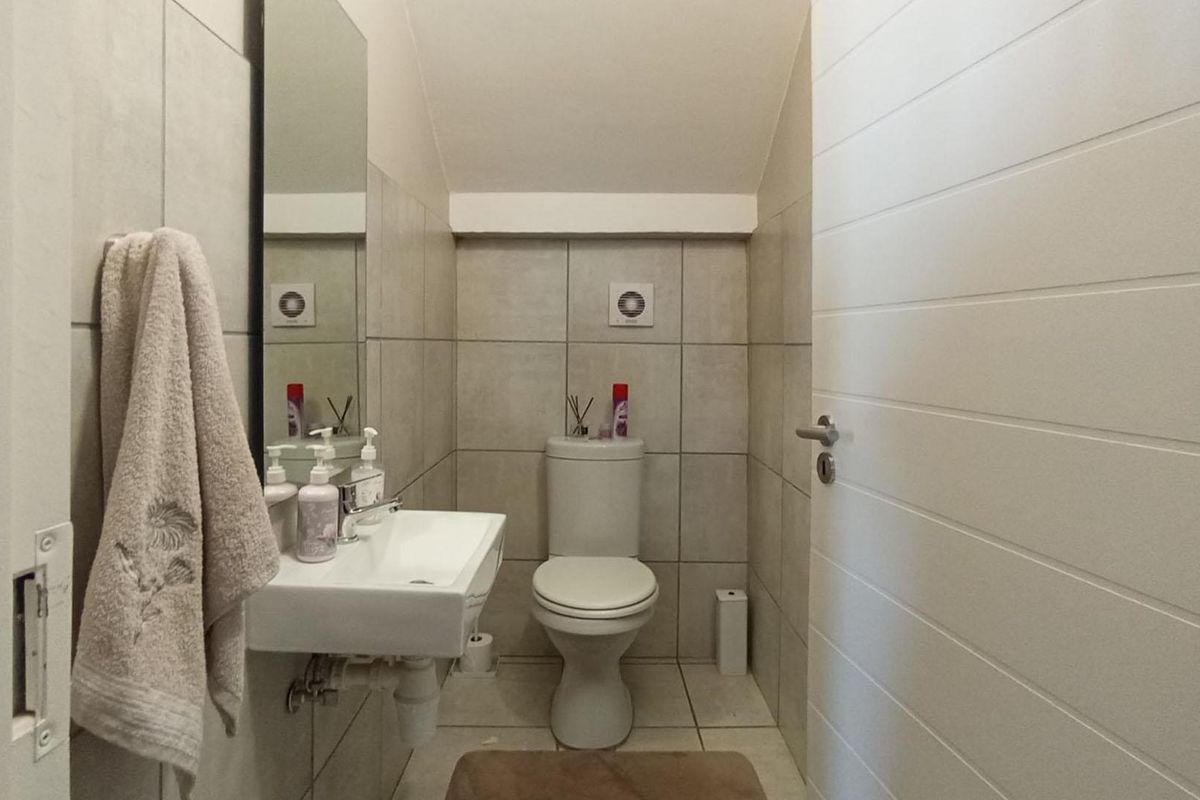 A compact guest bathroom featuring neutral wall tiles, a wall-mounted basin, and a standard toilet.