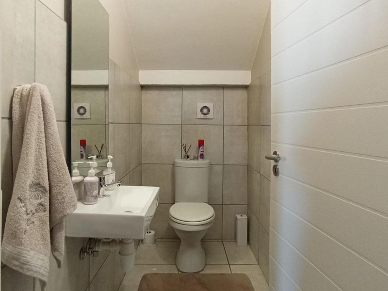 A compact guest bathroom featuring neutral wall tiles, a wall-mounted basin, and a standard toilet.