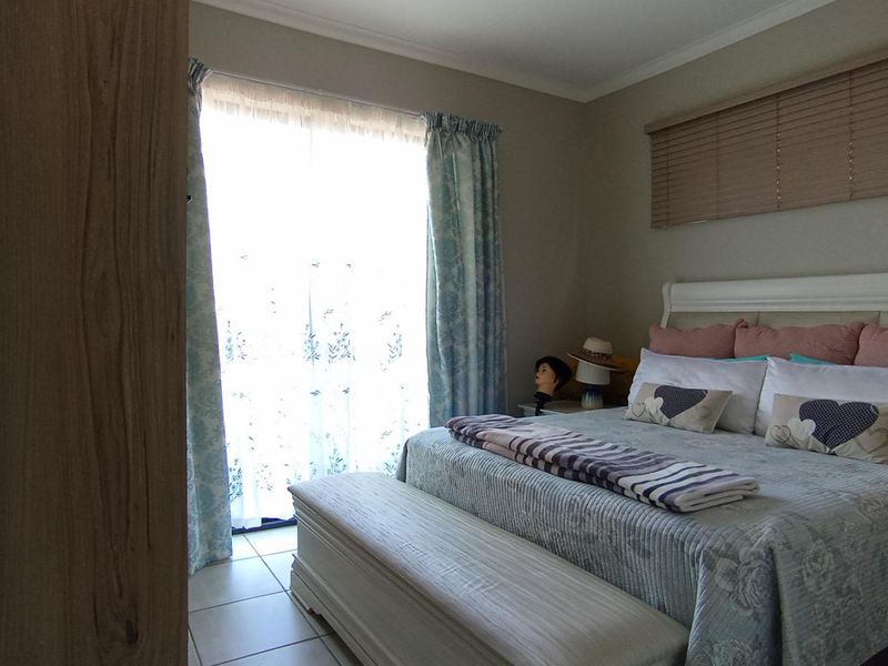 A well-maintained bedroom featuring tiled flooring, a sliding glass door providing natural light, and fitted venetian blinds.