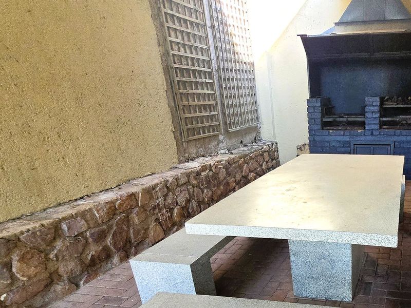 Covered outdoor patio area featuring a built-in brick braai, stone-clad wall accents, and durable paved flooring, ideal for alfresco dining and entertaining.