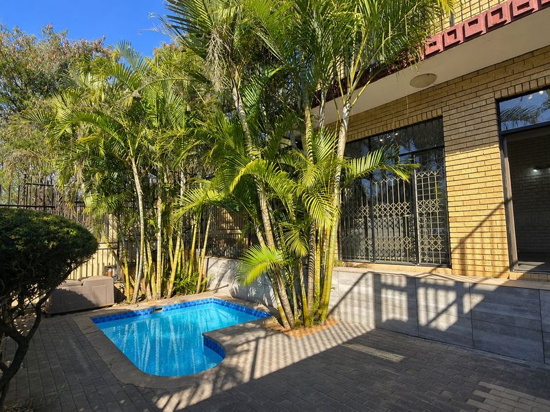 A private outdoor pool area featuring brick paving, established palm trees, and direct access to the home through sliding glass doors with security gates.