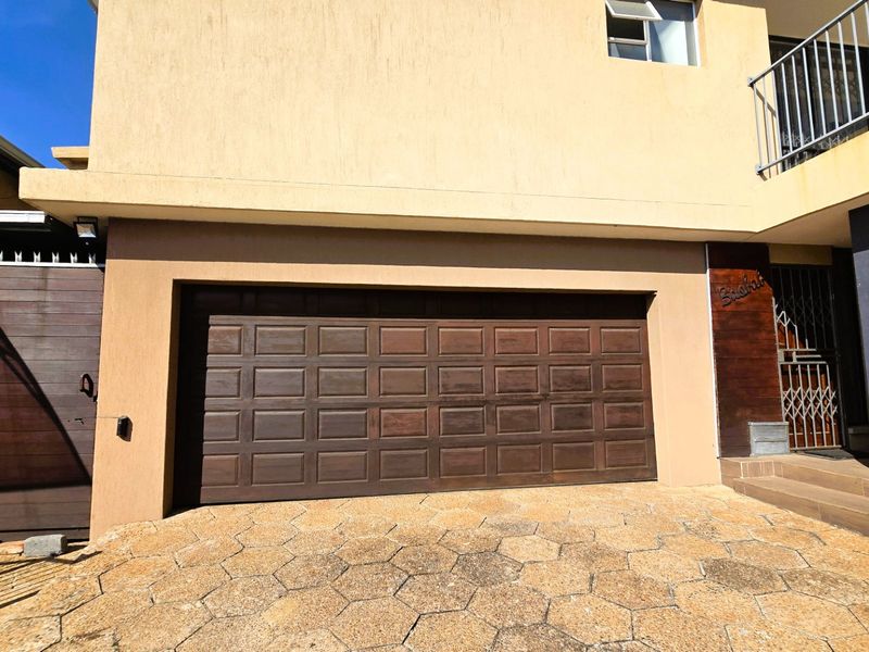 Front elevation of the property featuring a double garage door, paved driveway, and a secure entrance area with balcony access above.