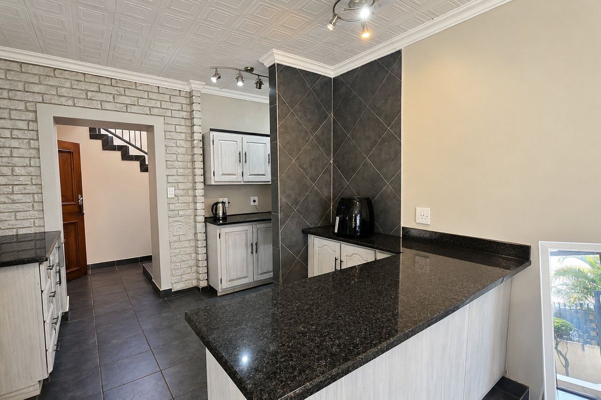 A well-maintained kitchen featuring granite countertops, built-in cabinetry, and a distinctive brick feature wall, leading to an adjacent staircase area.