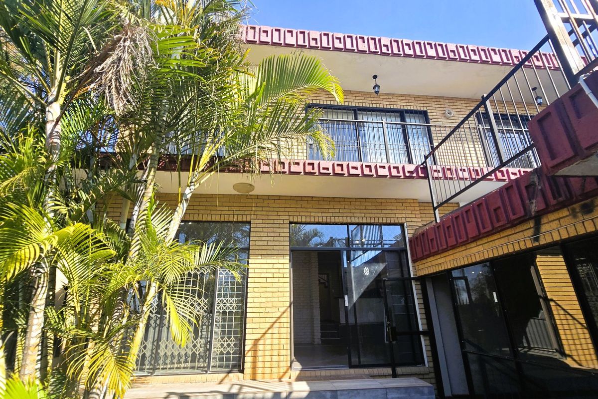 Rear elevation of a two-story brick house featuring a balcony with metal railings and large sliding glass doors with security gates.