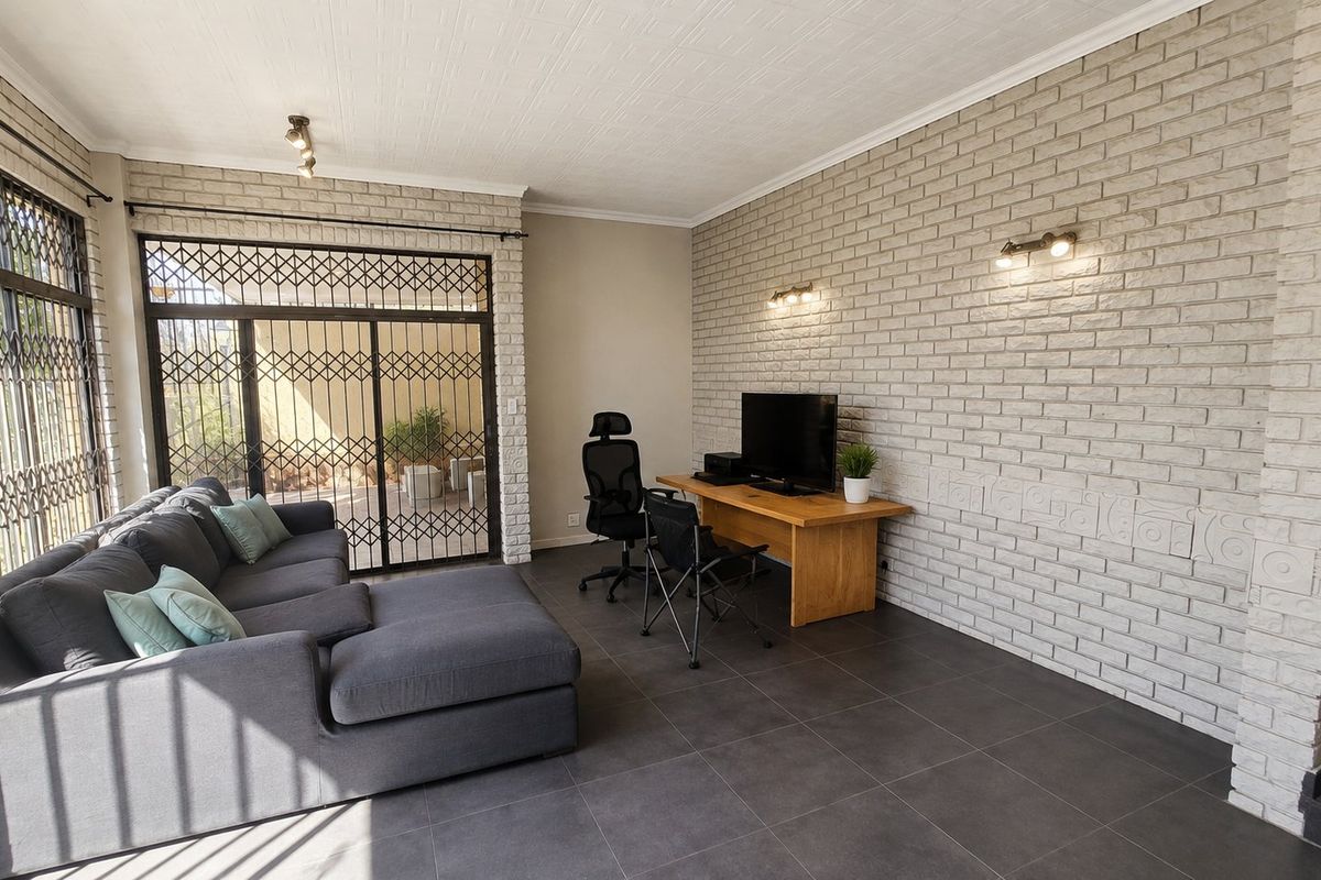 A living area featuring a textured exposed brick wall, large format floor tiles, and secure sliding glass doors leading to an outdoor space.
