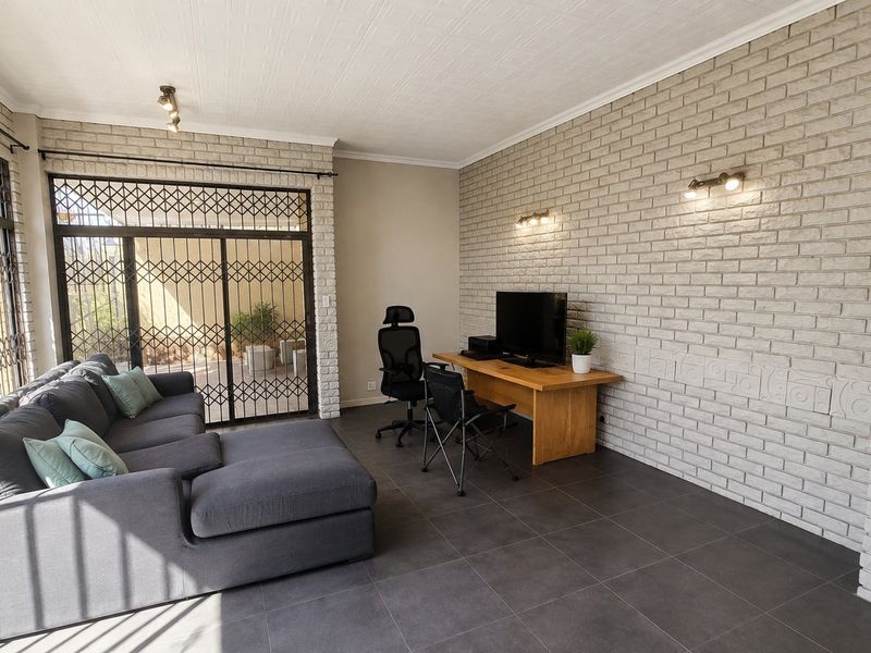 A living area featuring a textured exposed brick wall, large format floor tiles, and secure sliding glass doors leading to an outdoor space.