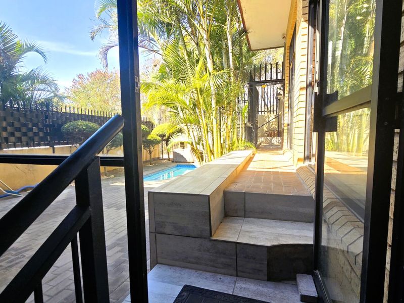 A view from a doorway looking out onto a paved patio area with tiled steps leading to a swimming pool and garden.