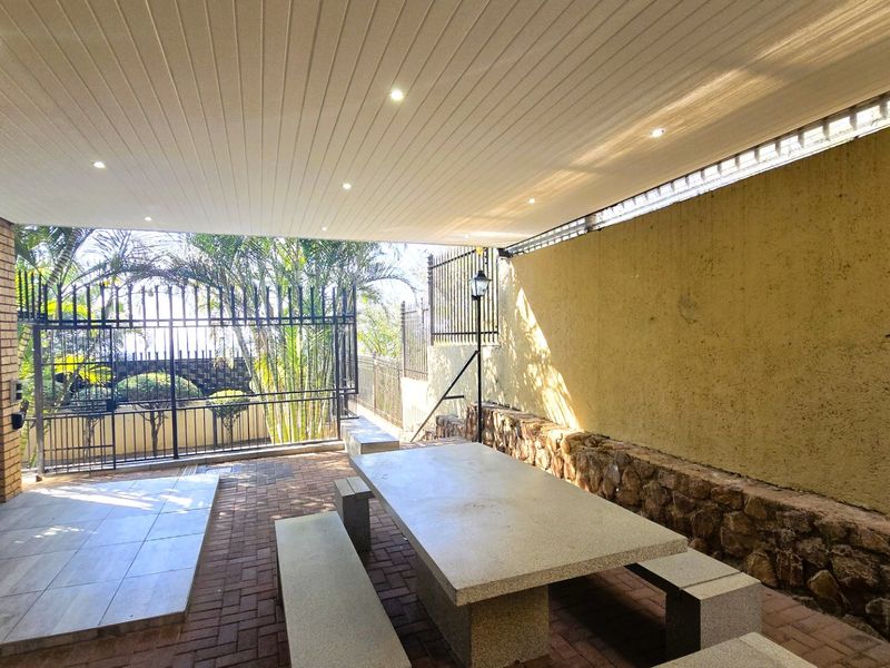 A covered outdoor patio area featuring brick paving, stone wall accents, recessed ceiling lighting, and secure metal fencing, ideal for alfresco dining.