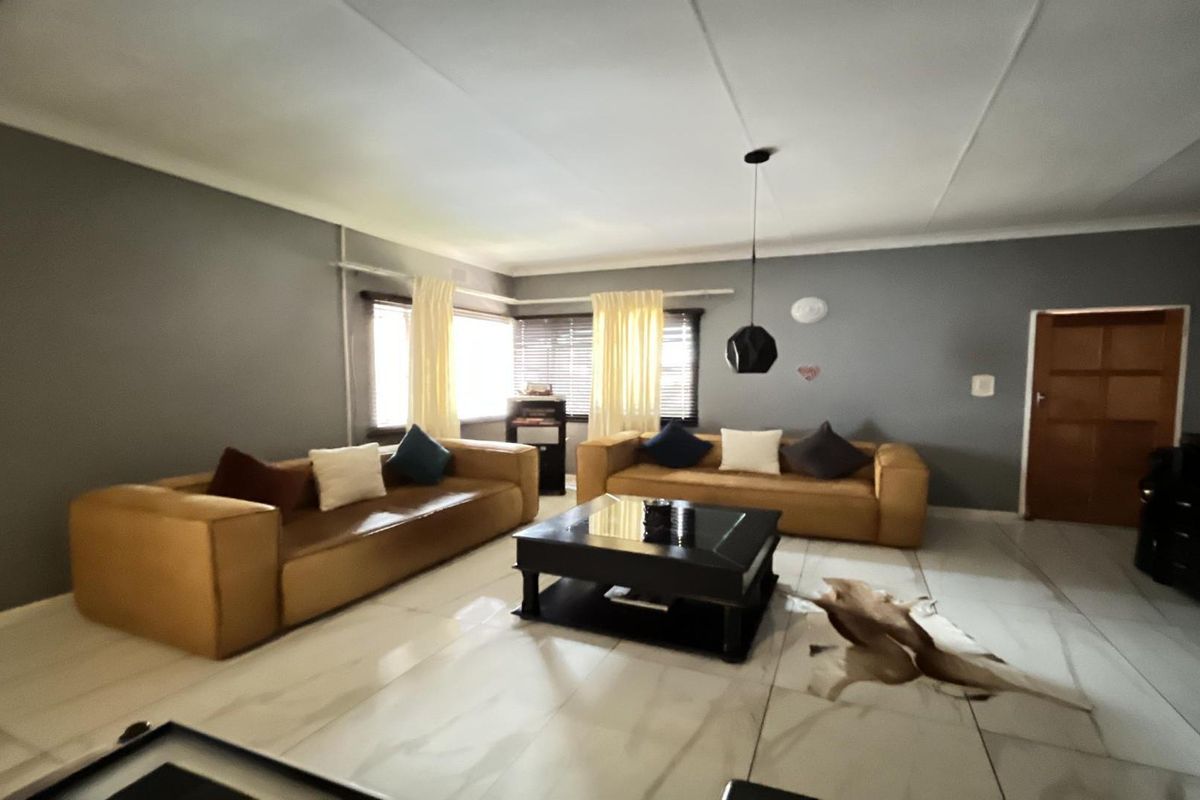 A spacious living room featuring large format floor tiles, neutral grey walls, and a coved ceiling with modern pendant lighting.