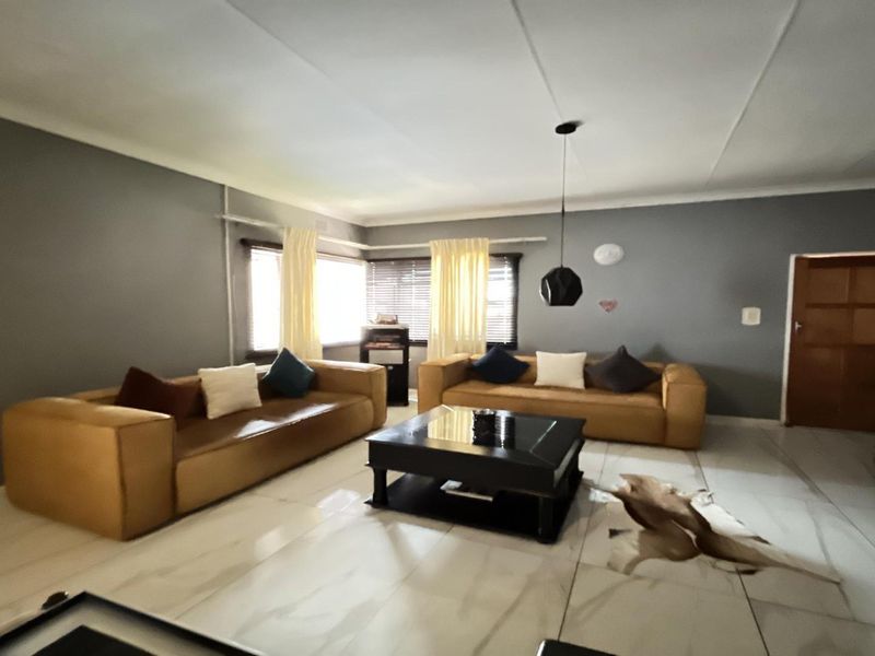 A spacious living room featuring large format floor tiles, neutral grey walls, and a coved ceiling with modern pendant lighting.