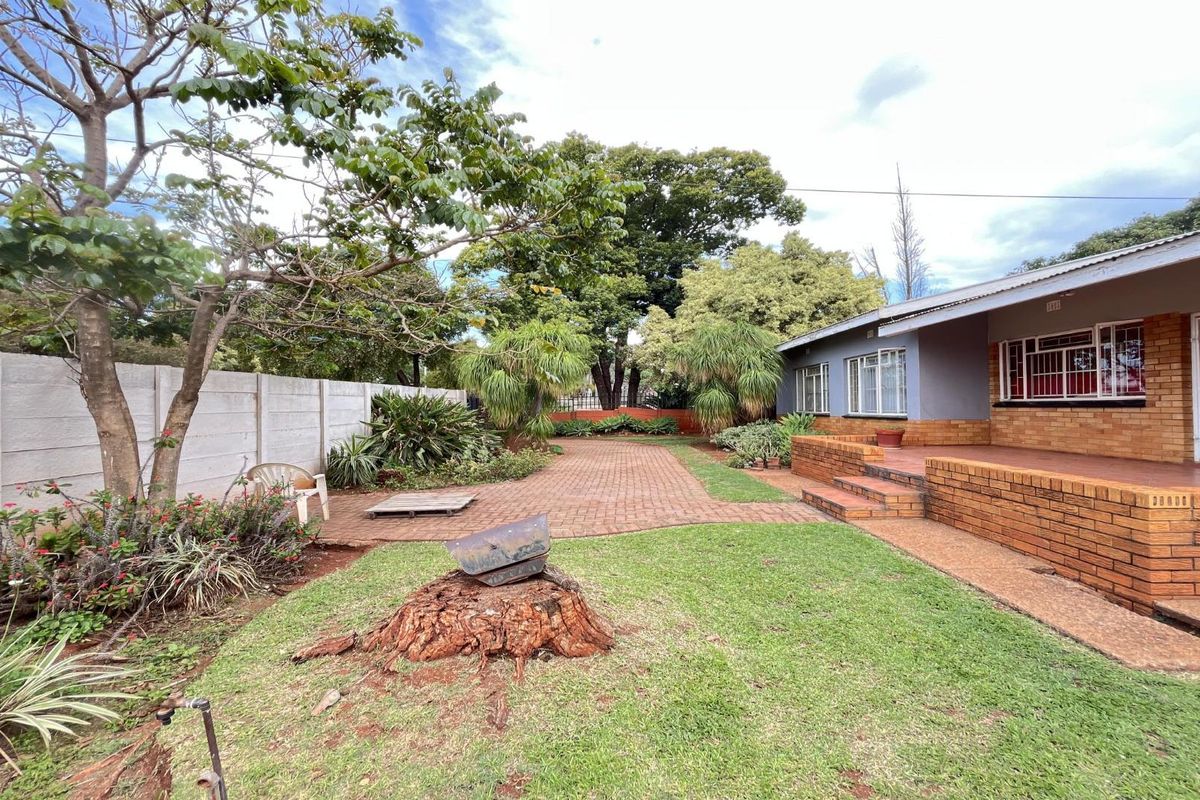 A rear exterior view featuring a brick patio, landscaped garden area, and a secure brick-built house facade with security gates.