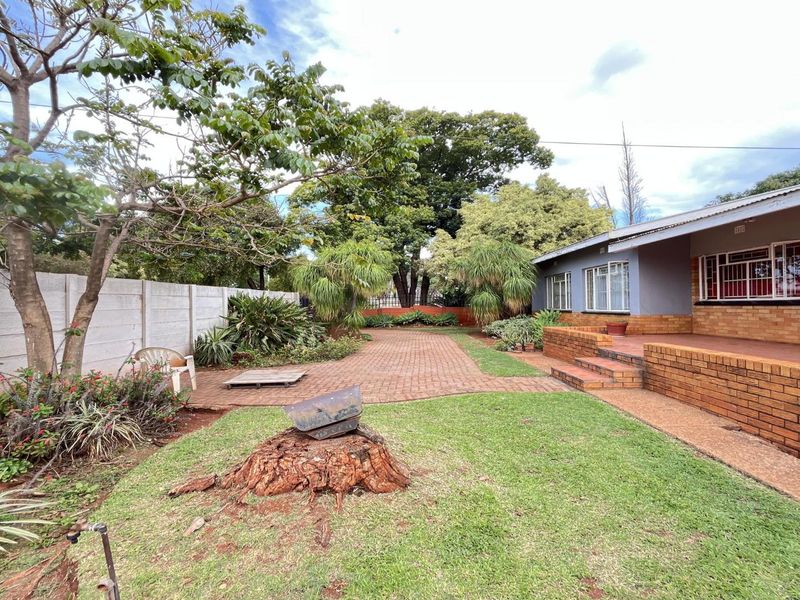 A rear exterior view featuring a brick patio, landscaped garden area, and a secure brick-built house facade with security gates.