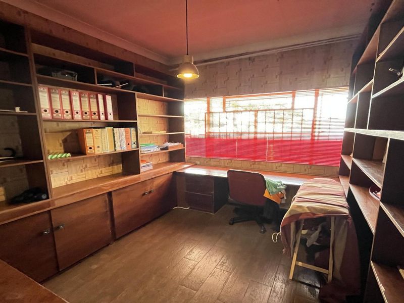 A dedicated home office featuring extensive built-in wooden cabinetry, shelving, and a spacious integrated desk area with tiled flooring.