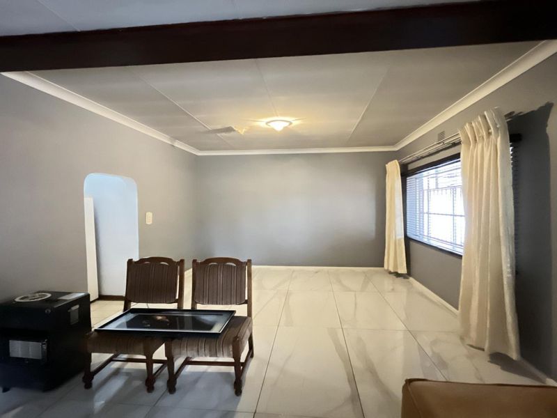 Spacious living room featuring large format tiled flooring, an exposed ceiling beam, and a neutral grey color palette with an arched entryway.