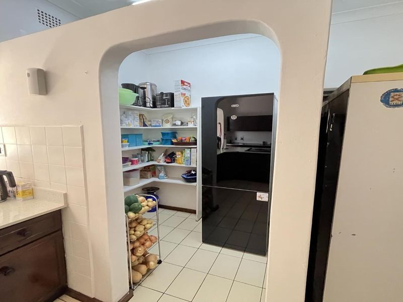 A functional scullery or pantry area featuring built-in shelving, tiled flooring, and an arched entryway connecting to the main kitchen space.