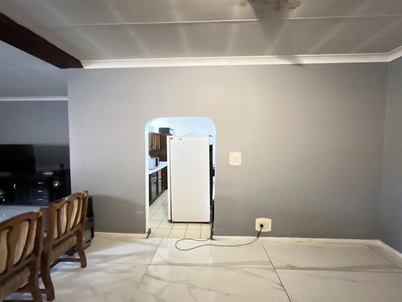 Open plan living area featuring large format floor tiles, coved ceilings, and an arched doorway leading to the kitchen area.