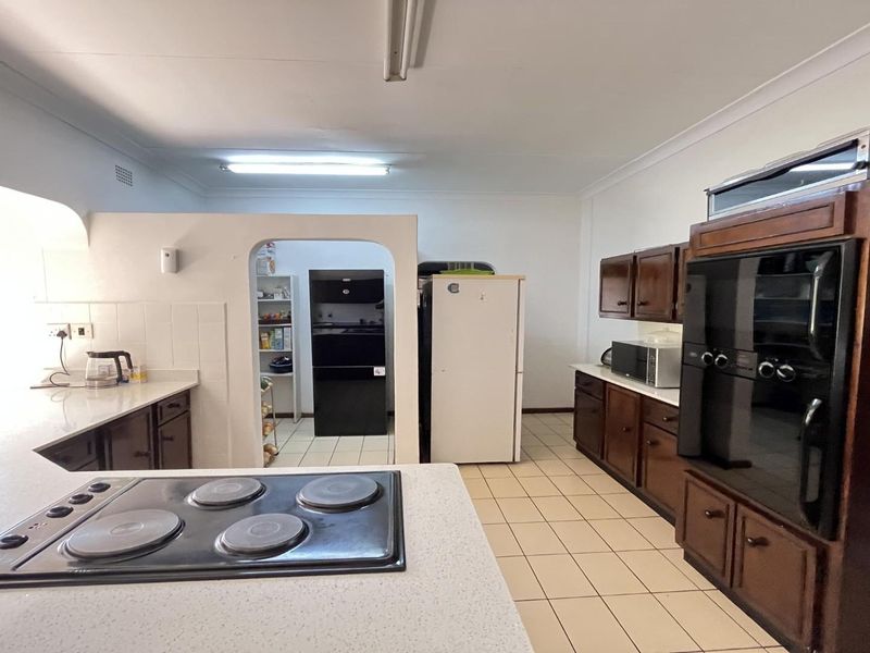 Spacious kitchen featuring dark wood cabinetry, built-in oven and hob, tiled flooring, and an adjoining scullery area.