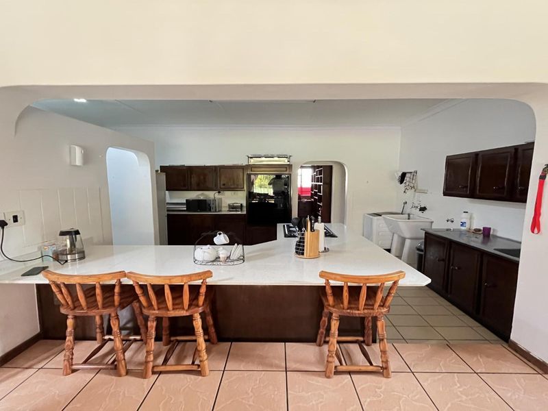 Spacious kitchen featuring a large central island with breakfast bar, dark wood cabinetry, and tiled flooring, offering a functional layout for cooking and dining.