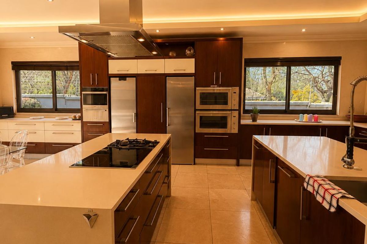 Modern, spacious kitchen featuring dual islands, high-end built-in appliances, stone countertops, and sophisticated recessed and cove lighting.