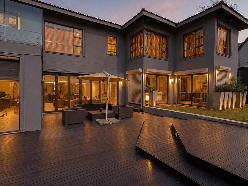 Spacious rear exterior featuring extensive timber decking, modern glass sliding doors, and integrated lighting, creating a seamless transition between indoor and outdoor living spaces.