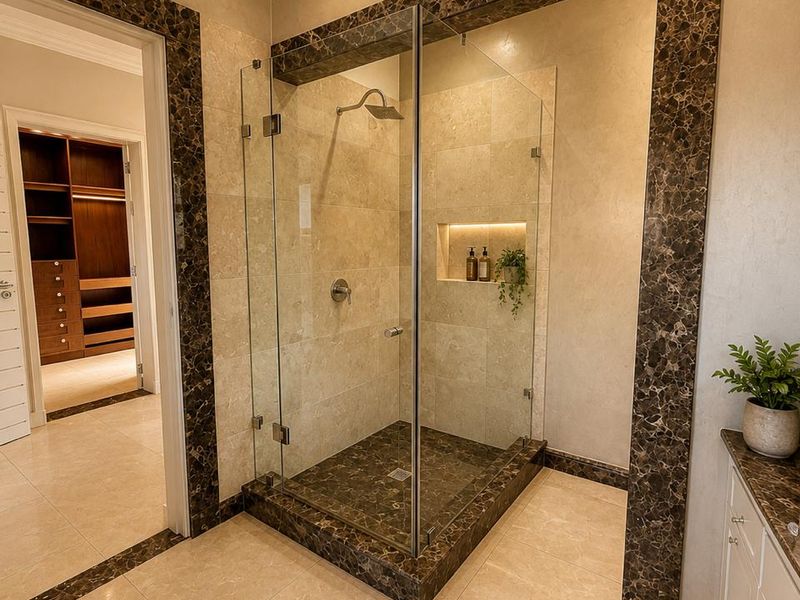 Modern bathroom featuring a frameless glass shower with marble accents, built-in niche lighting, and high-quality stone tile finishes throughout.