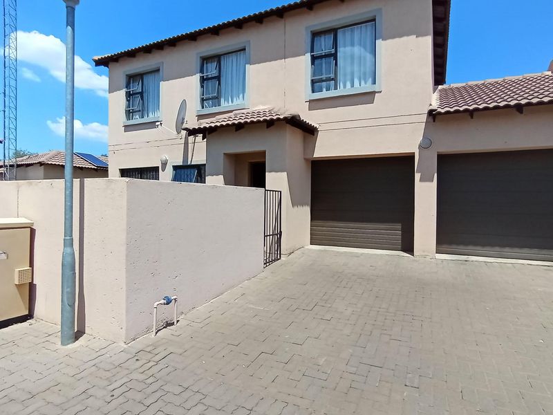 Front elevation of a double-storey townhouse featuring a paved driveway, double garage, and neutral exterior wall finish.