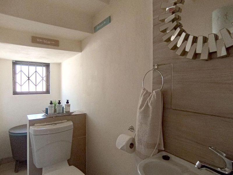 A compact bathroom featuring a toilet, basin with faucet, and a decorative tiled feature wall with a security-grille window.