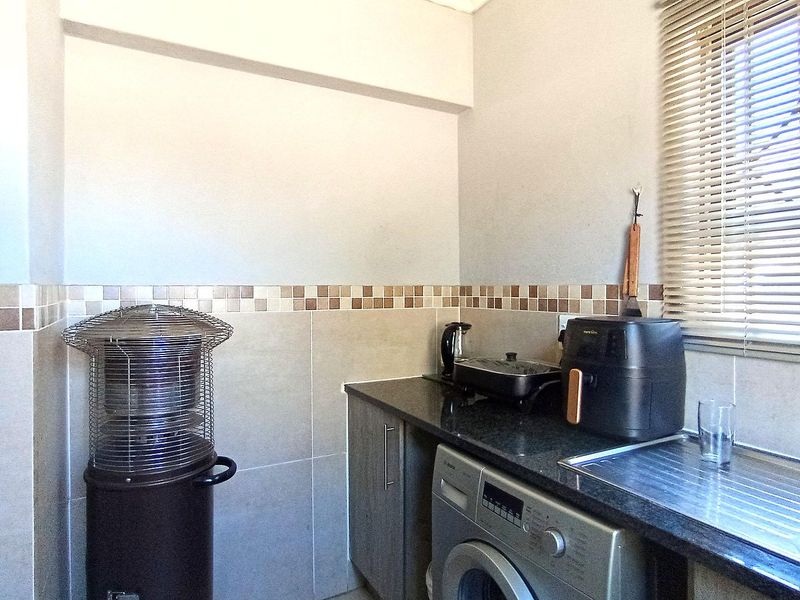 A functional laundry area featuring granite countertops, a stainless steel sink, built-in cabinetry, and a tiled backsplash with venetian blinds.