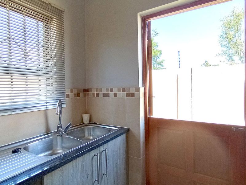 A functional scullery area featuring a double stainless steel sink, tiled splashback, laminate cabinetry, and a stable door providing direct outdoor access.