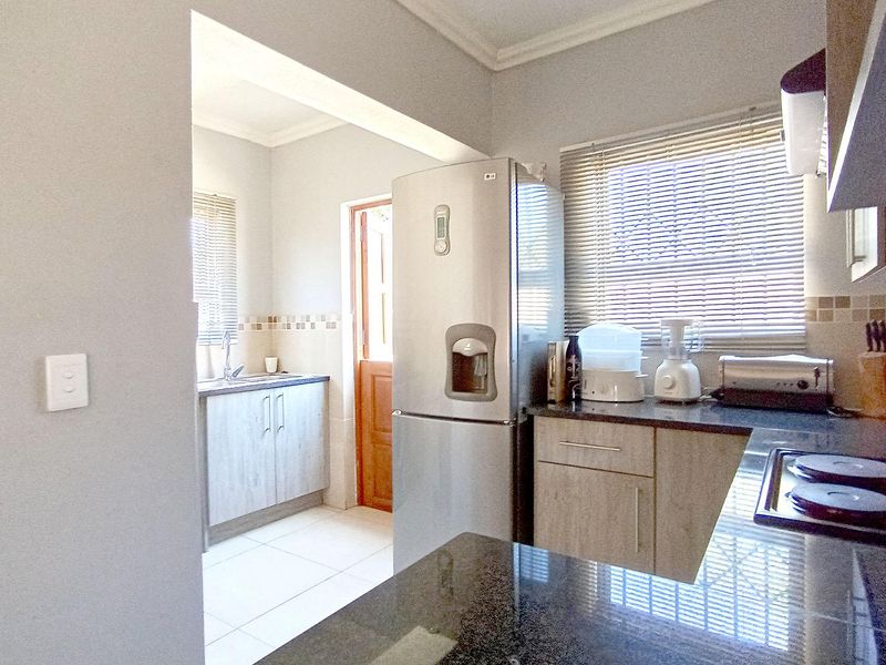 A functional kitchen featuring granite countertops, built-in cabinetry, and an electric hob, with a separate scullery area and tiled flooring.