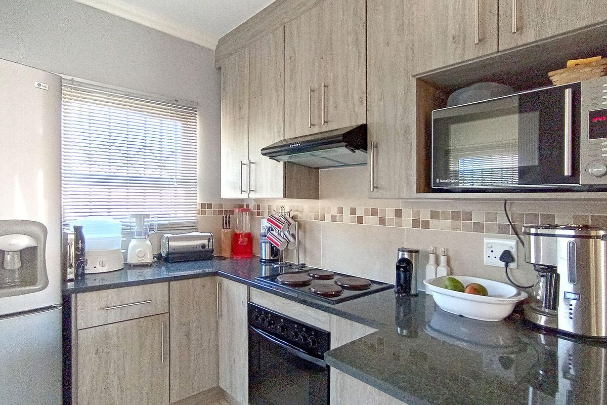 A functional kitchen featuring wood-look cabinetry, granite countertops, a built-in oven and hob, and a tiled backsplash.
