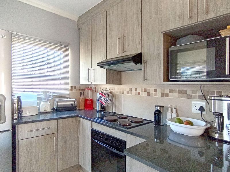 A functional kitchen featuring wood-look cabinetry, granite countertops, a built-in oven and hob, and a tiled backsplash.