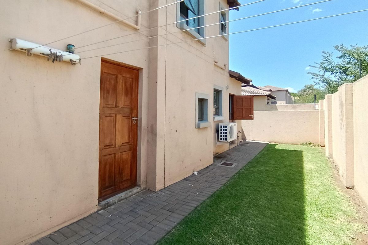 Rear exterior view of the townhouse featuring a paved walkway, small lawn area, boundary wall, and an installed air conditioning unit.