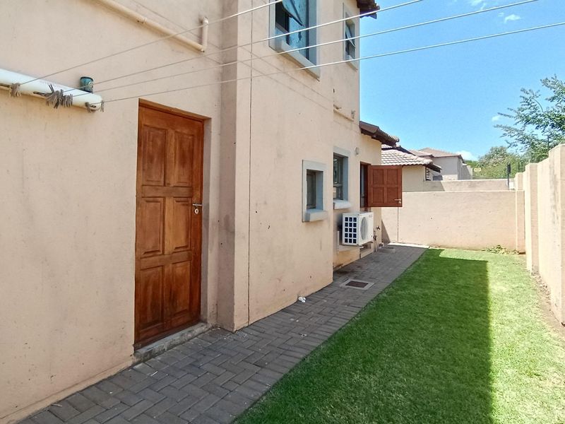 Rear exterior view of the townhouse featuring a paved walkway, small lawn area, boundary wall, and an installed air conditioning unit.