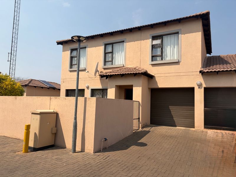 Front exterior view of a double-story townhouse featuring a paved driveway, integrated garage, and neutral rendered facade.