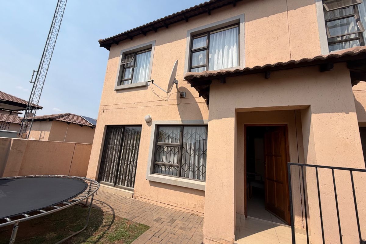 Rear exterior view of the townhouse featuring a paved patio area, sliding glass doors with security gates, and a tiled roof.
