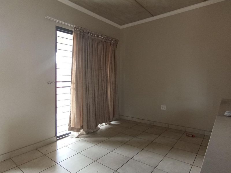 An open-plan living area featuring tiled flooring, an exposed concrete ceiling, and a sliding door with security gate leading to the exterior.