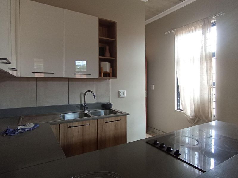 Modern kitchen featuring sleek cabinetry, stone countertops, a double sink, and a built-in electric hob, offering a clean and functional workspace.
