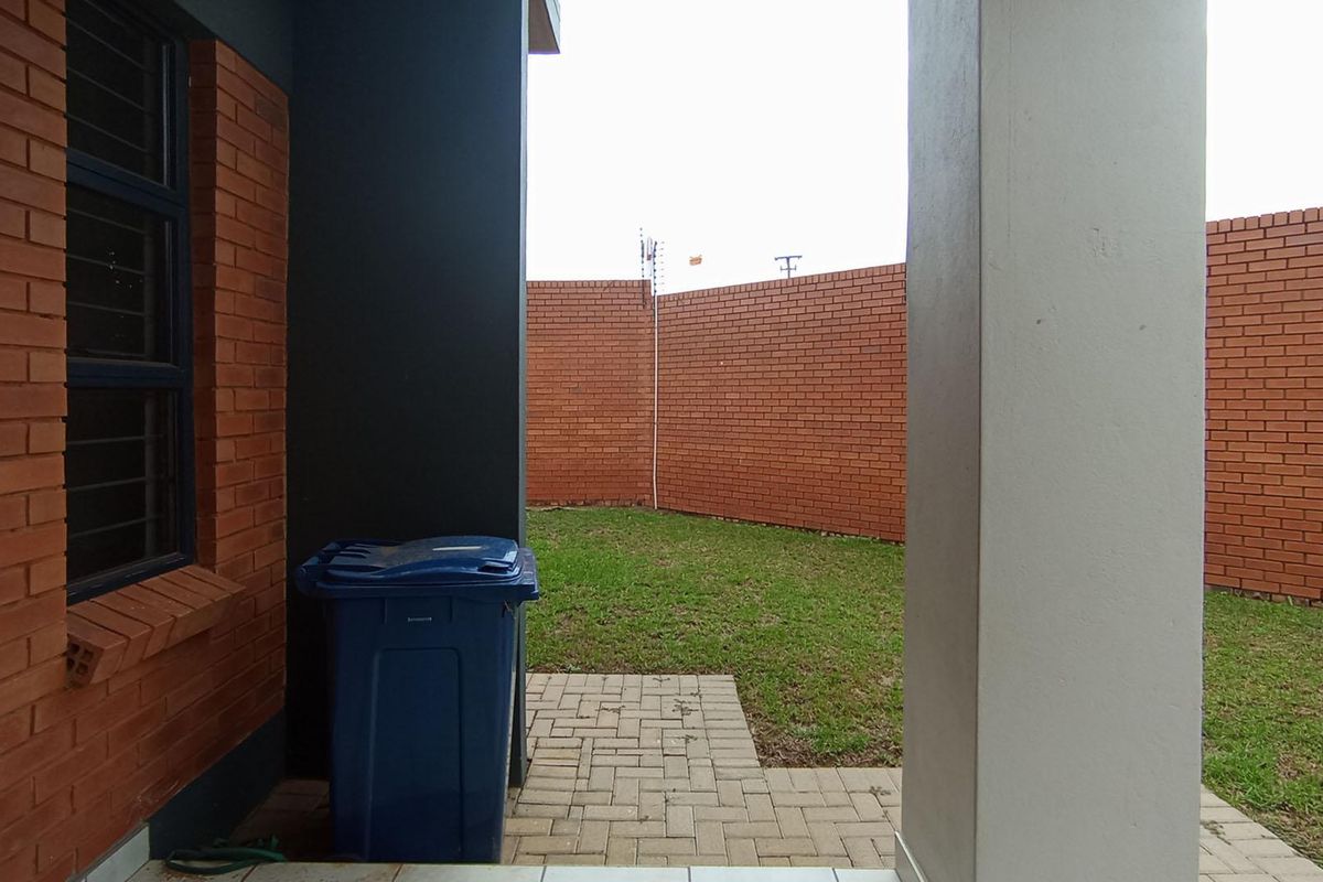 A private rear garden area featuring a paved walkway, lawn, and high brick boundary walls for added privacy.