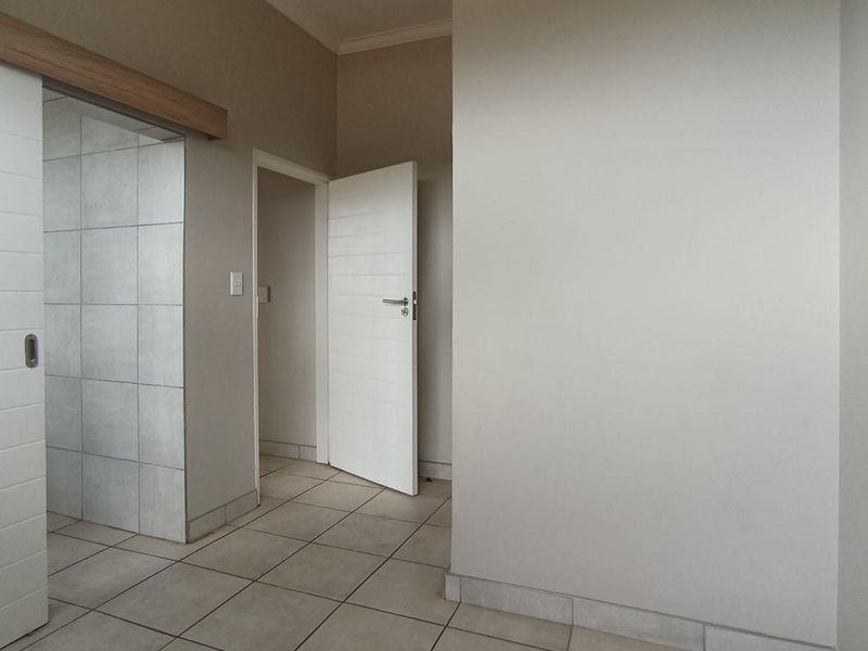 A clean, neutral-toned hallway featuring tiled flooring, a sliding door, and access to adjacent rooms.