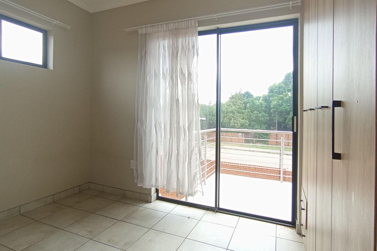 A bright, empty bedroom featuring tiled flooring, built-in cupboards, and a sliding glass door providing direct access to an outdoor patio area.