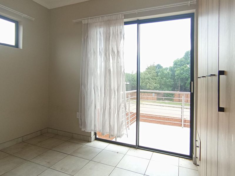 A bright, empty bedroom featuring tiled flooring, built-in cupboards, and a sliding glass door providing direct access to an outdoor patio area.