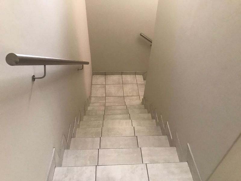 A functional staircase featuring neutral ceramic floor tiles and a modern stainless steel handrail, providing access between levels.