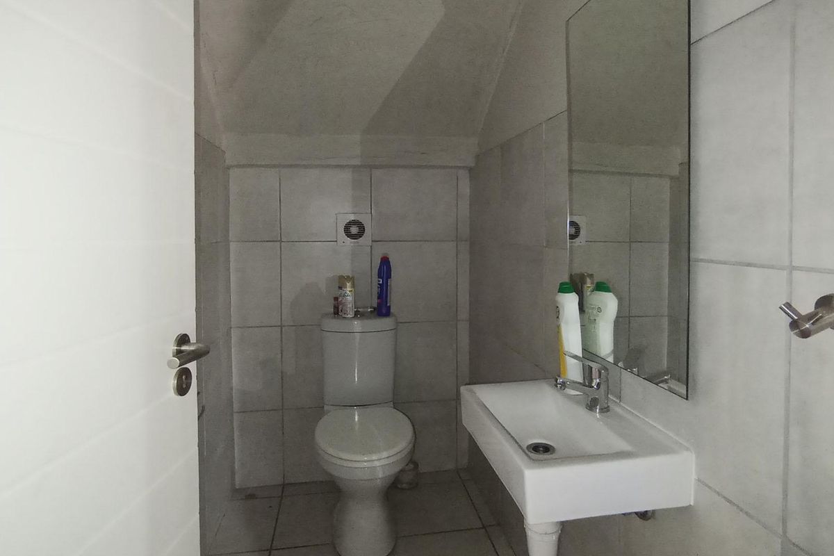 A compact guest bathroom featuring a wall-mounted basin, toilet, and neutral wall tiling under a sloped ceiling.
