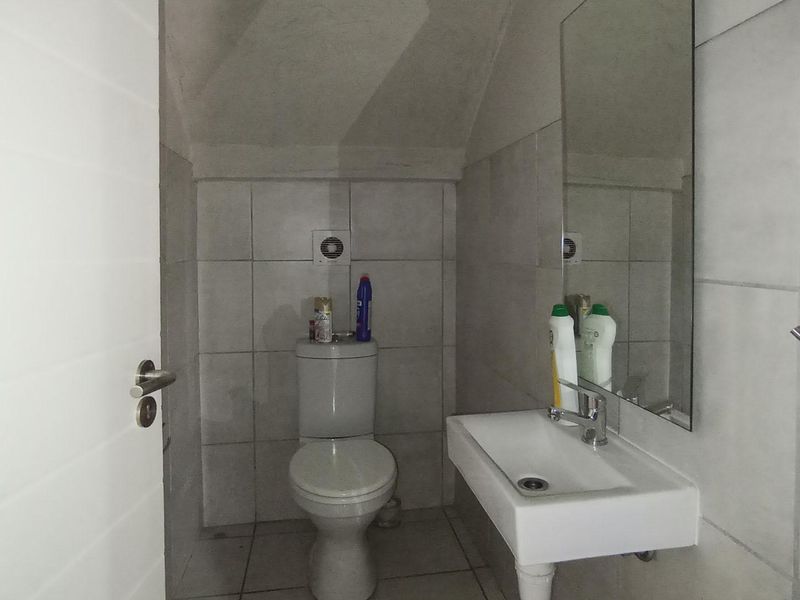 A compact guest bathroom featuring a wall-mounted basin, toilet, and neutral wall tiling under a sloped ceiling.