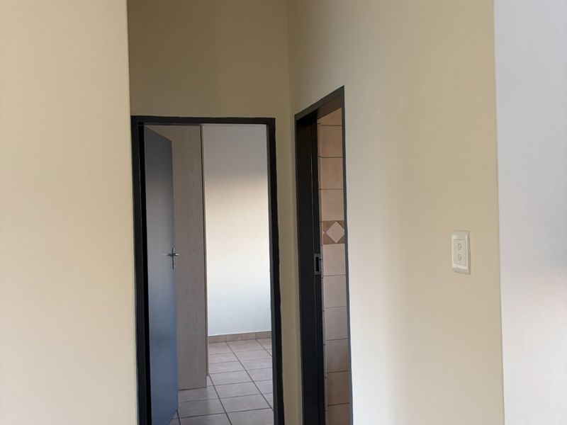 A clean, empty hallway featuring neutral wall paint and tiled flooring, providing access to adjacent rooms within the apartment.