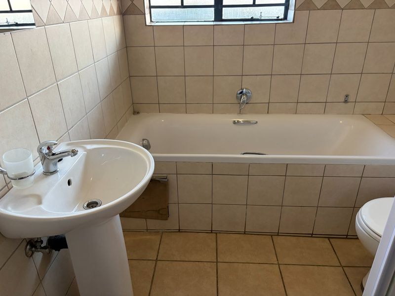 A functional bathroom featuring a pedestal basin, built-in bathtub, and toilet, finished with neutral ceramic wall and floor tiles.
