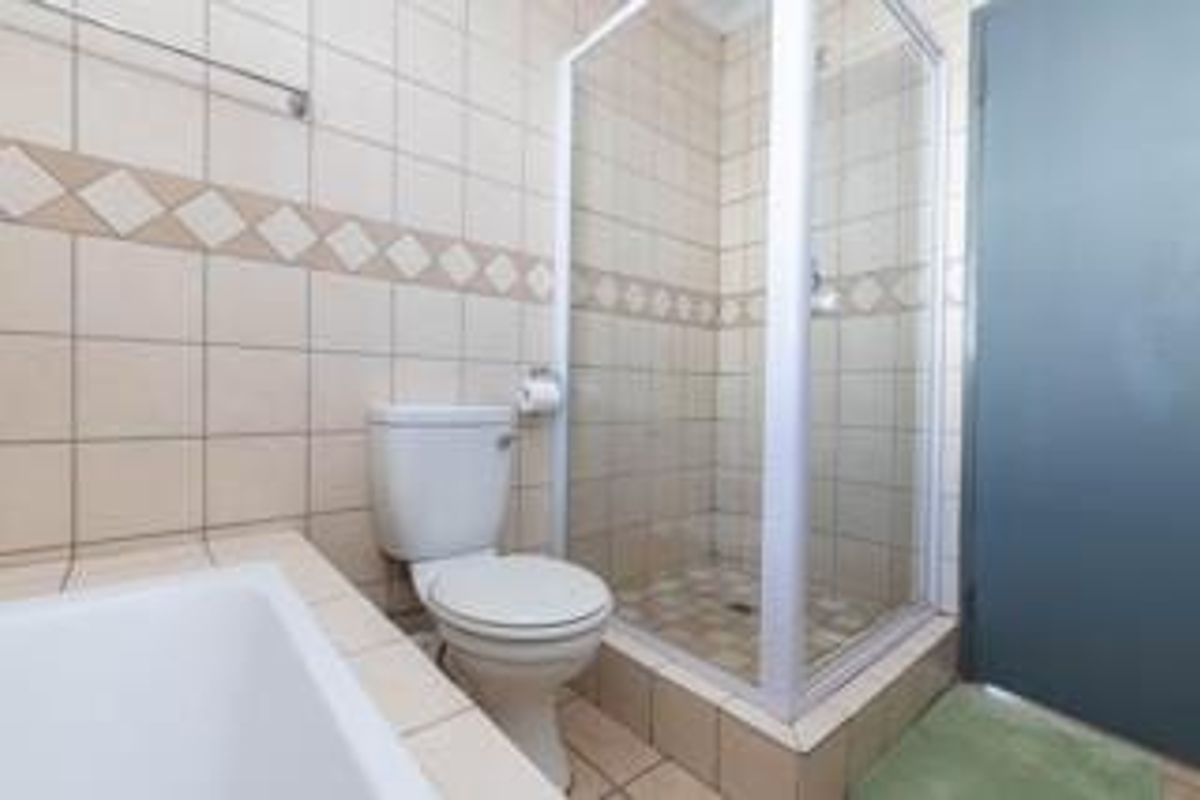 A functional bathroom featuring a shower enclosure, toilet, and neutral wall and floor tiling.