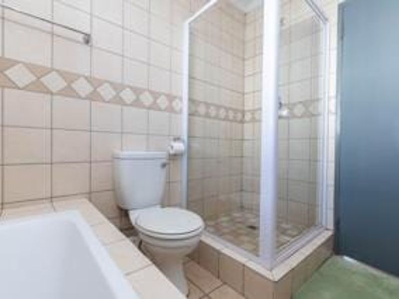 A functional bathroom featuring a shower enclosure, toilet, and neutral wall and floor tiling.